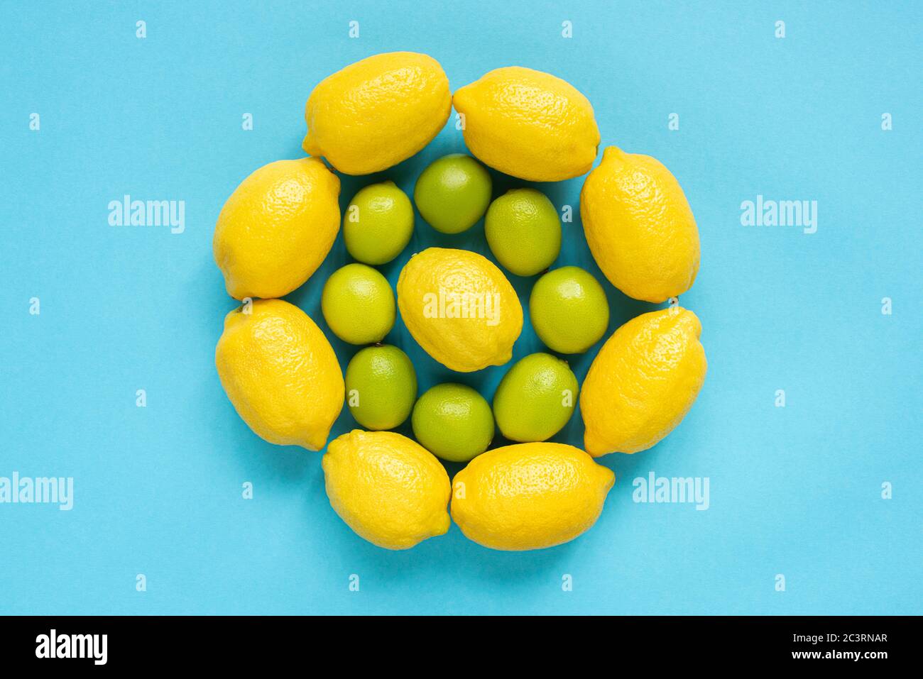 vista superior de limones amarillos maduros y limas dispuestas en círculos sobre fondo azul Foto de stock