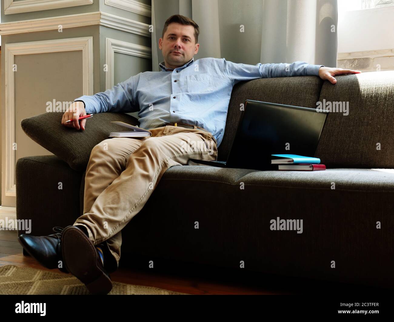 Concepto de teletrabajo. Freelancer está sentado en un sofá con un ordenador portátil y papeles. Foto de stock