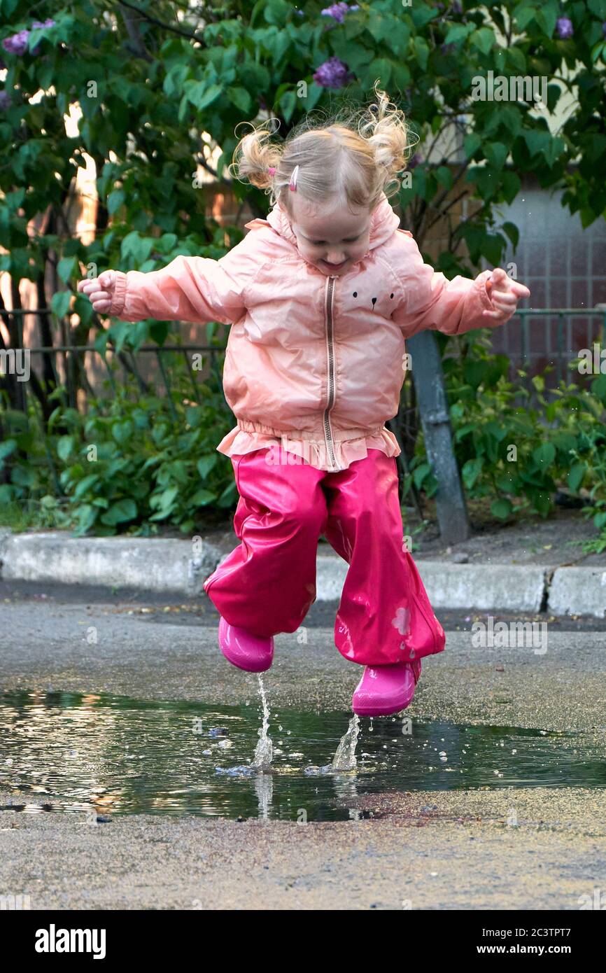 Niño feliz saltando en charco en abrigo impermeable. Una chica se divierte  en el clima de lluvia con un brillante impermeable Fotografía de stock -  Alamy
