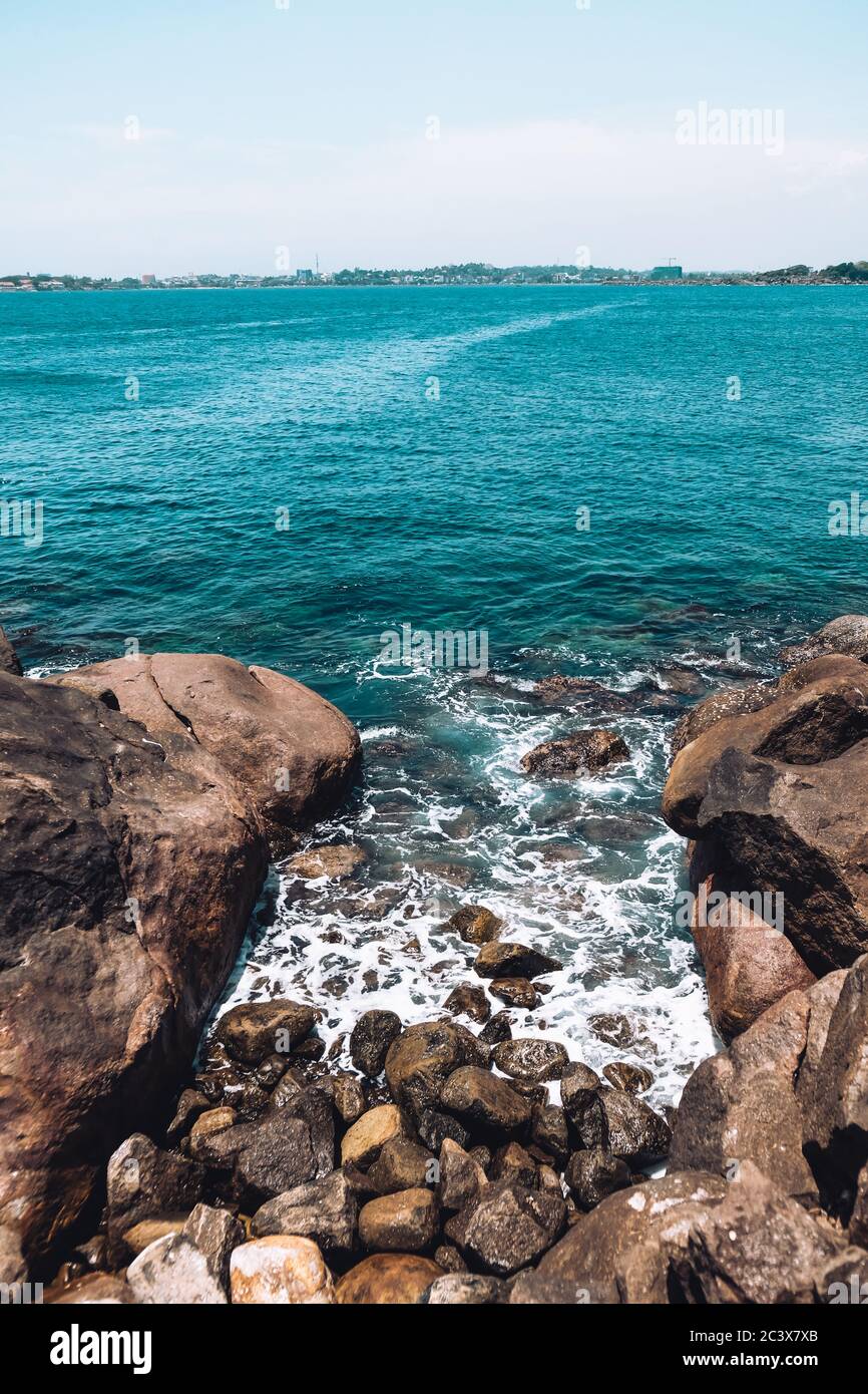 Olas azules rompiendo en rocas y guijarros cerca de la playa de la selva. Buen color del agua, mar áspero y horizonte. Lugar tranquilo sin turistas Foto de stock