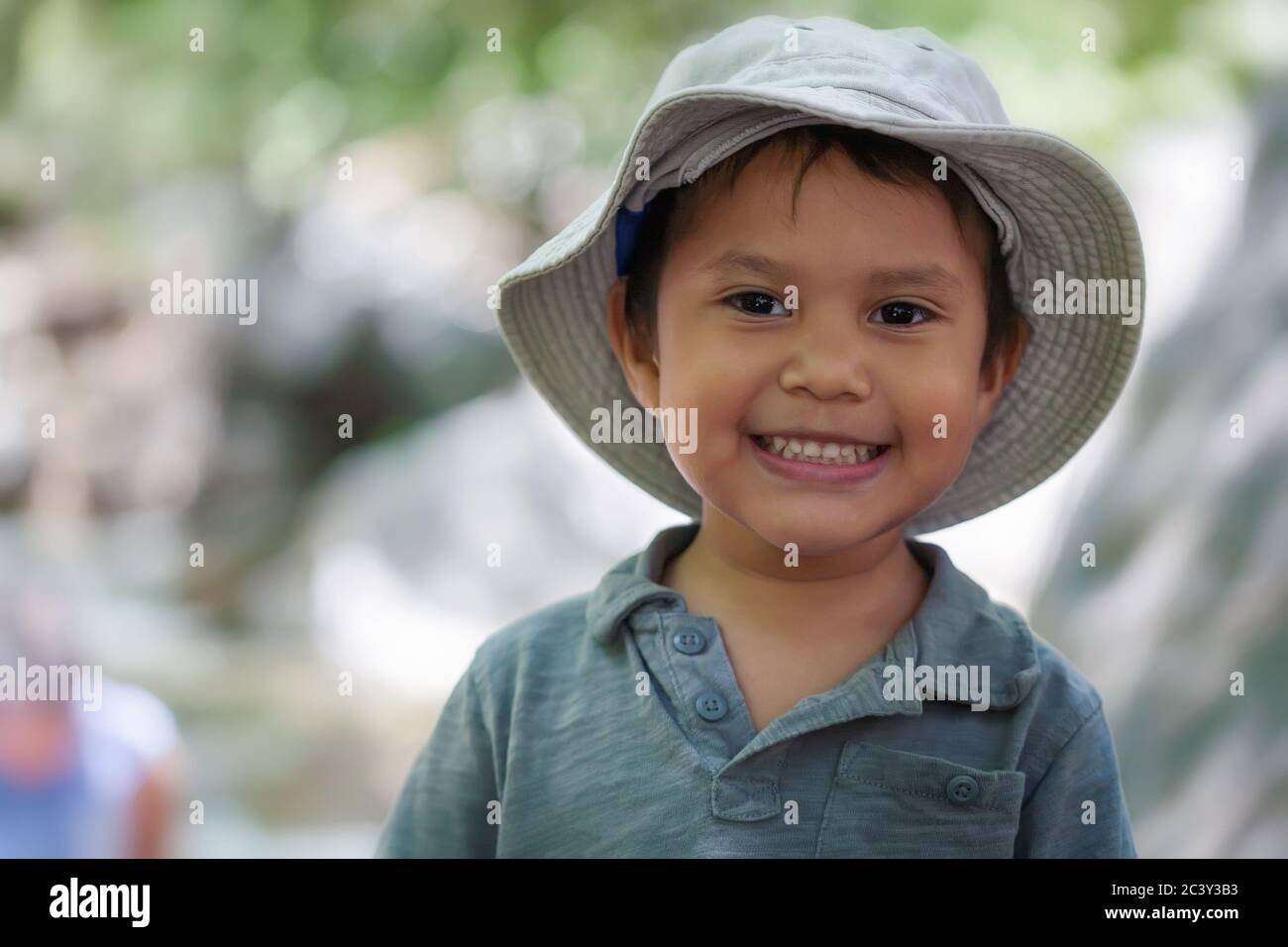 Joven hispano vestido con un sombrero de pesca que sonríe y se ve feliz en un entorno natural al aire libre. Foto de stock