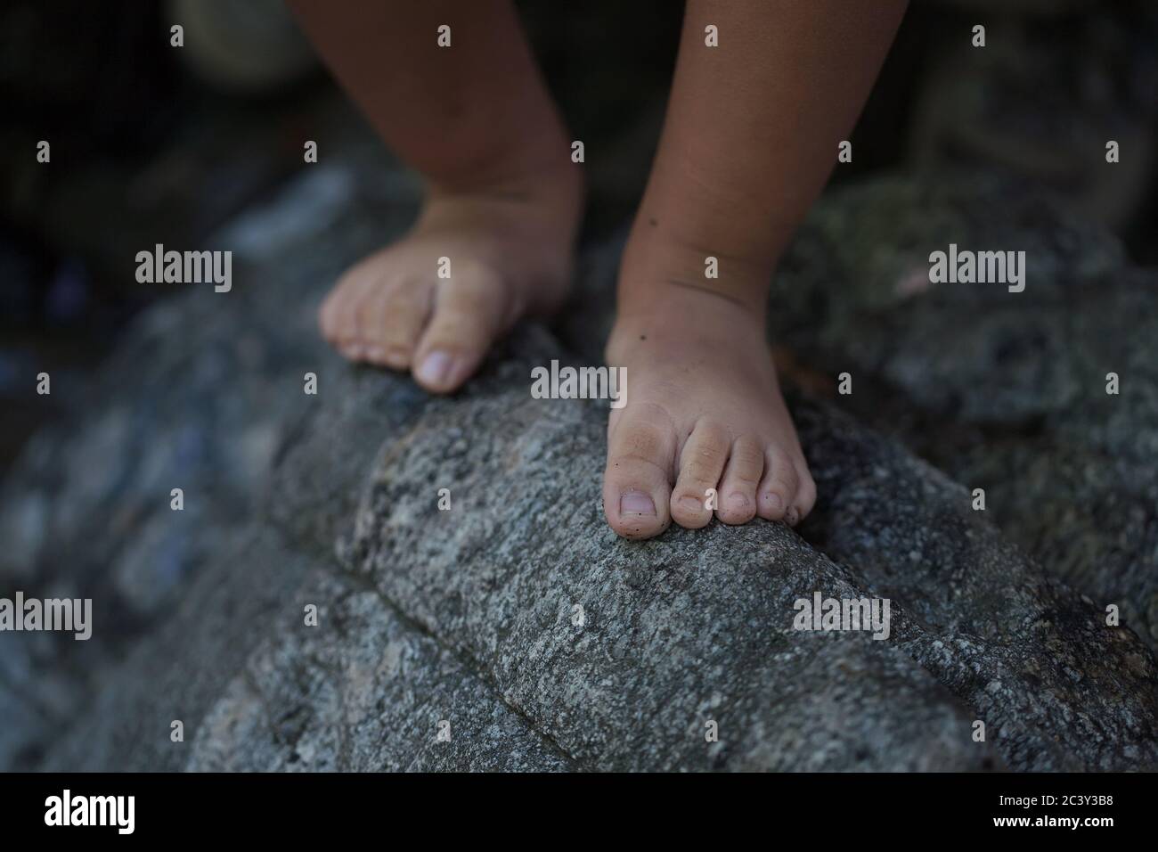 un cierre de un niño pequeño desnuda pies que se equilibra en el borde de una roca áspera para transmitir una situación peligrosa. Foto de stock
