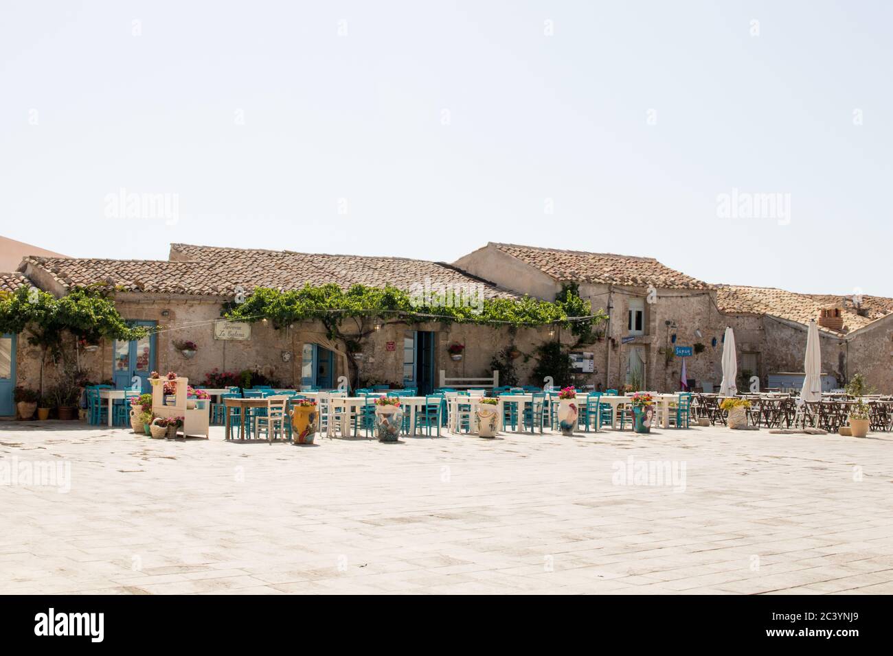 Plaza de marzamemi en sicilia. Restaurante con mesas azules y grandes macetas de flores Foto de stock