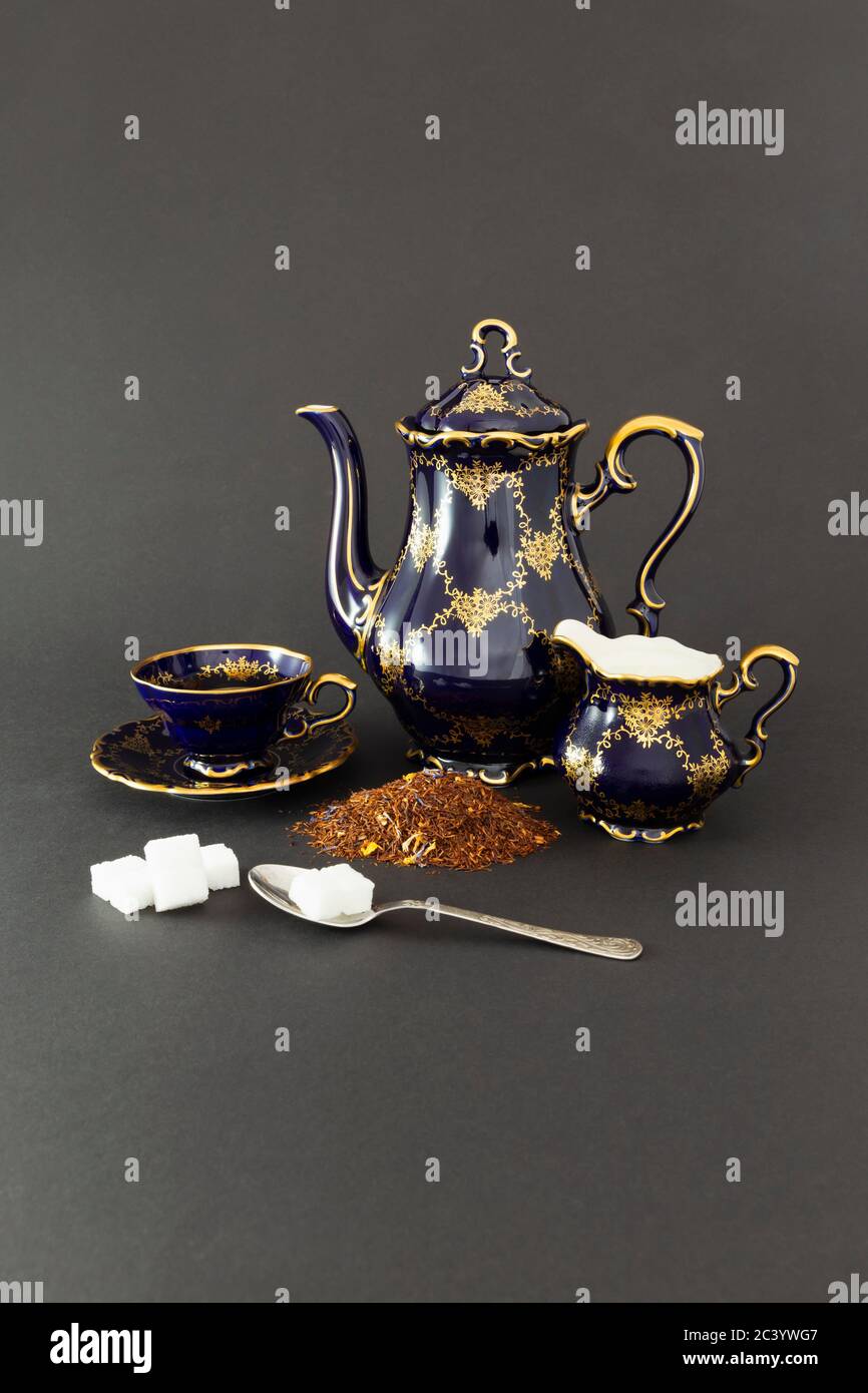 Vida con un hermoso juego de té de porcelana vintage color azul cobalto, cuchara con cubos de azúcar, jarra de leche y hojas de té secas. Foto de stock