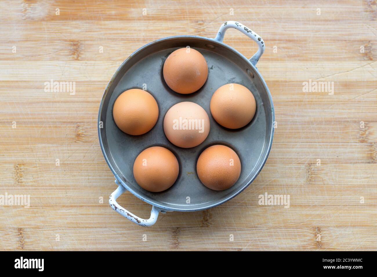 Seis huevos de gallina marrón fresca en una olla de metal o un cochero de huevo visto desde arriba en una mesa de madera con copyspace colocado en el centro Foto de stock