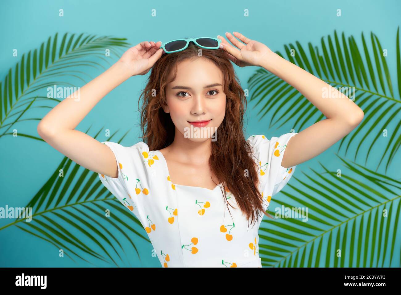 Mujer joven con hermoso maquillaje y hojas tropicales sobre fondo azul Foto de stock