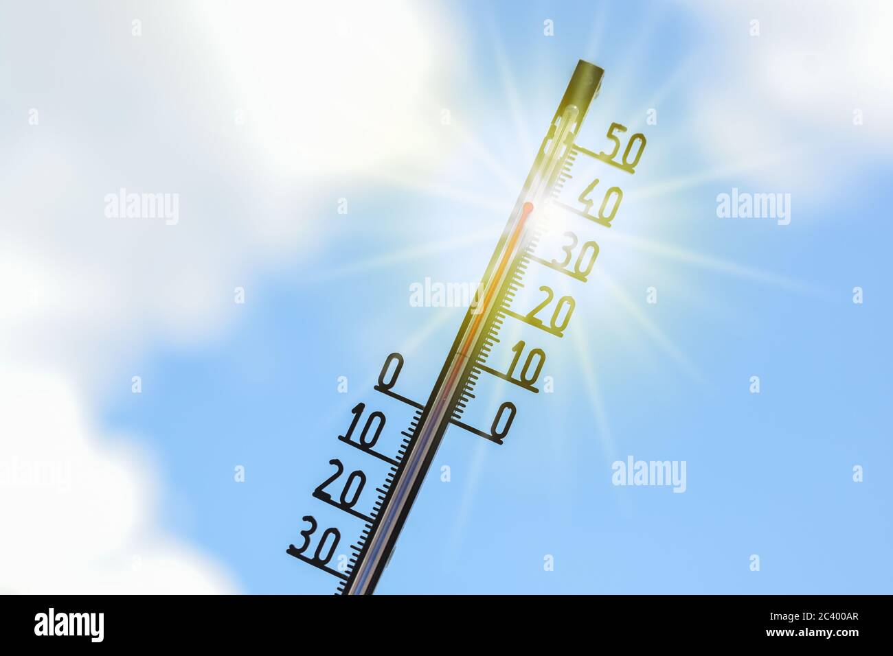 Termómetro muestra calor en la temporada de verano contra un cielo azul con nubes y rayos de sol, fenómeno meteorológico debido al calentamiento del clima con consecuencias s Foto de stock