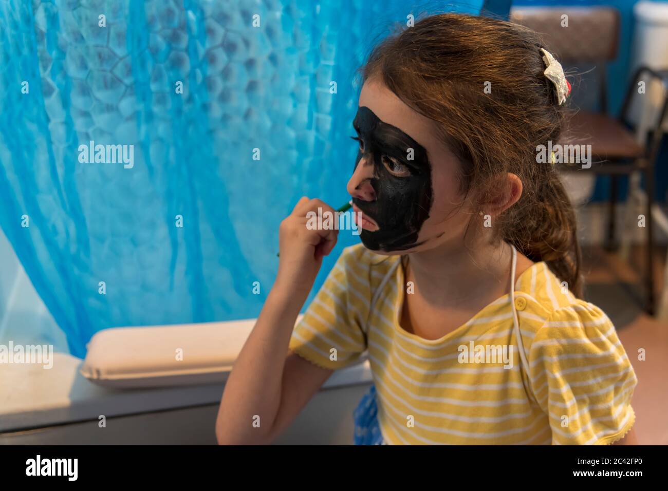 Una niña de una familia pobre y privada se está entreteniendo con pintura de cara Foto de stock
