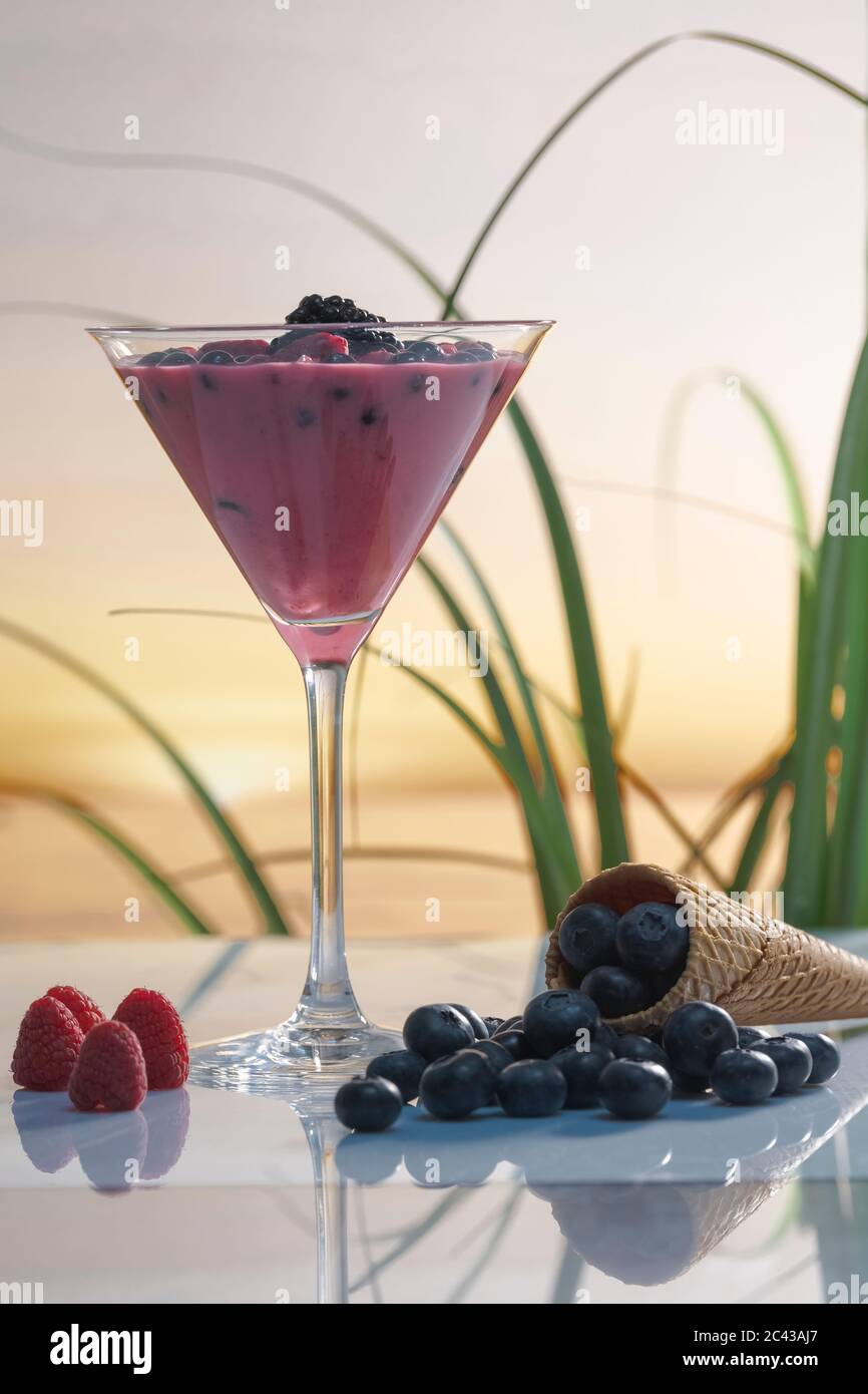 Martini de vidrio con batido de frutas y moras rodeadas de arándanos,  frambuesas y un cono de hielo sobre un fondo desenfocado. Vacaciones y h  Fotografía de stock - Alamy