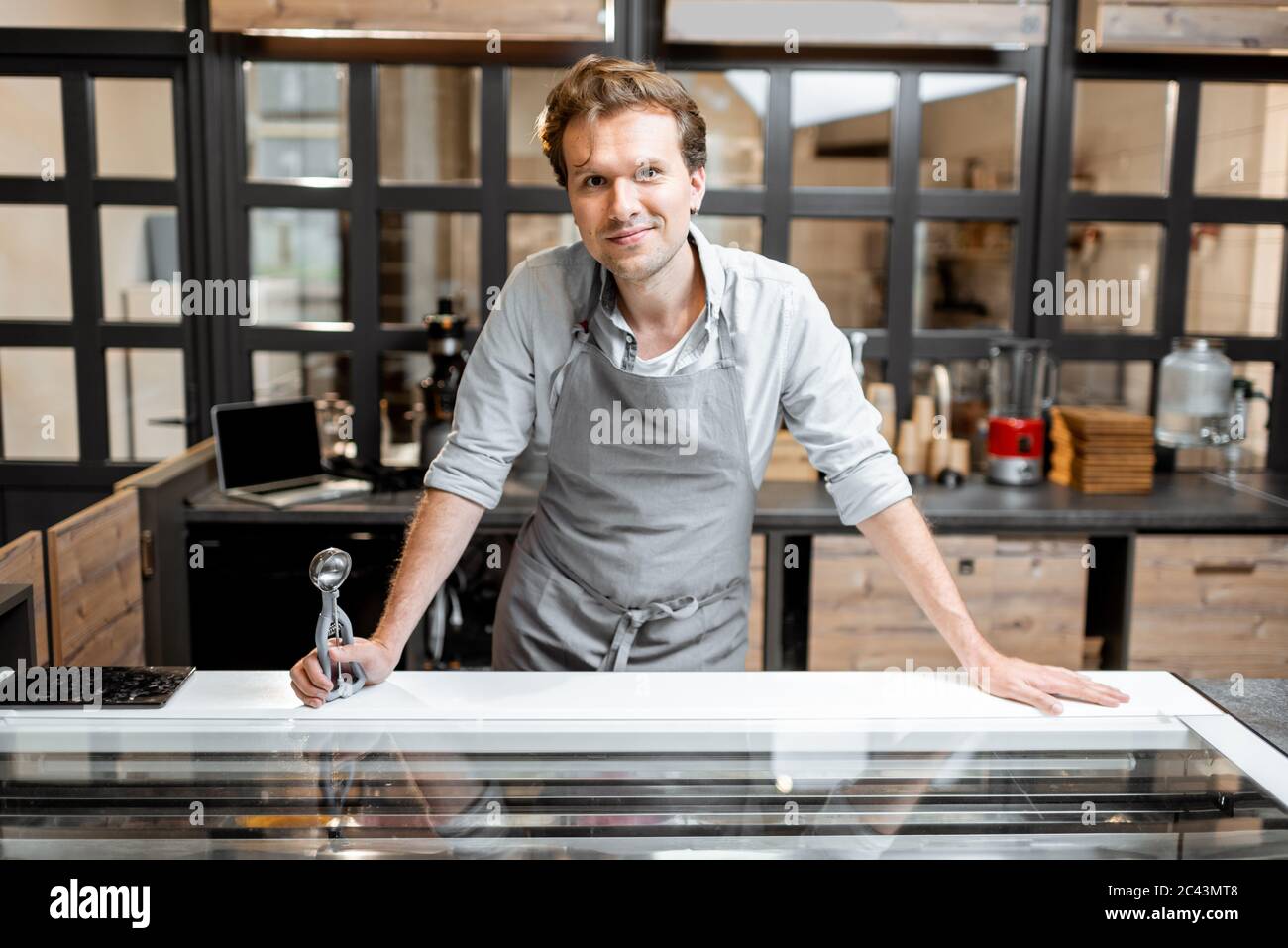 Retrato de un alegre vendedor en un delantal de pie detrás del mostrador de una pequeña tienda o cafetería. Concepto de pequeña empresa y trabajo en el campo de los servicios Foto de stock