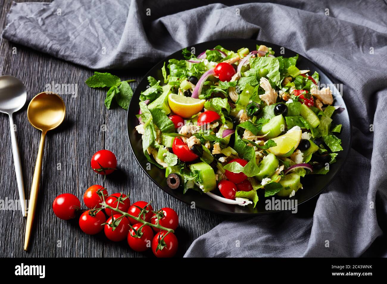 ensalada de carne de pollo, aceitunas, cebolla roja, tomates, pepino, menta, lechuga rociada con queso feta desmenuzado en un tazón negro, plato horizontal Foto de stock