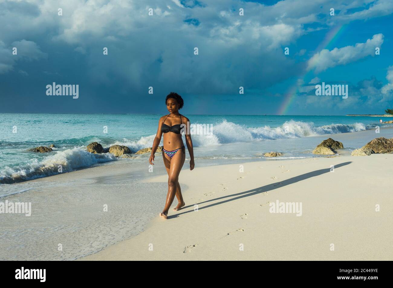 Mujer vistiendo bikini caminando por la playa de Grace Bay contra el cielo nublado, Providenciales, Islas Turcas y Caicos Foto de stock