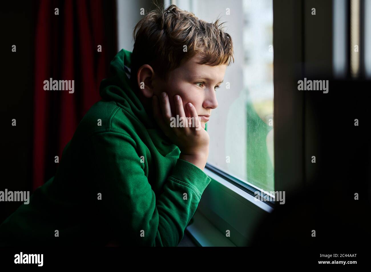Un niño aburrido mirando a través de la ventana de casa Foto de stock