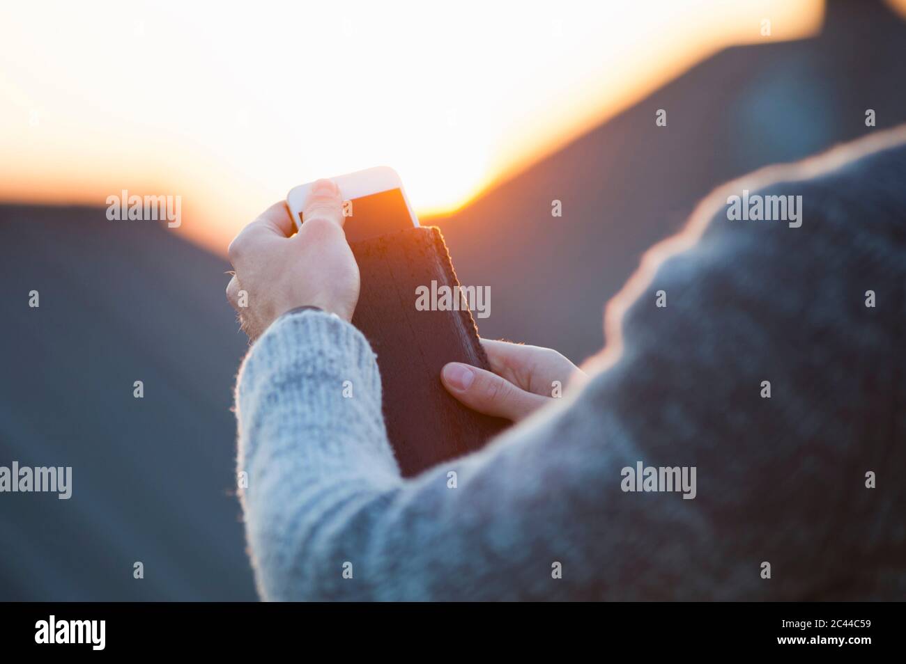 Imagen recortada de la mujer quitando el smartphone de la cubierta durante la puesta de sol Foto de stock