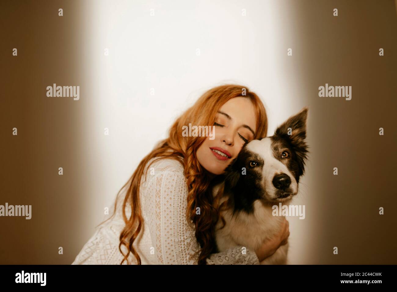 Mujer rubia en casa en pijama abrazando a su perro de collie de la frontera Foto de stock