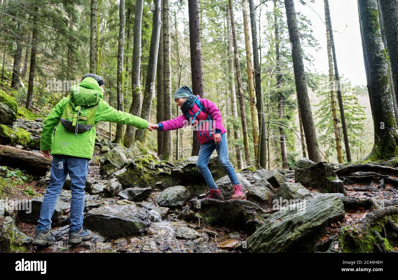 Niño ayudando a la hermana a cruzar un pequeño arroyo en el camino en la Selva Negra Norte Foto de stock