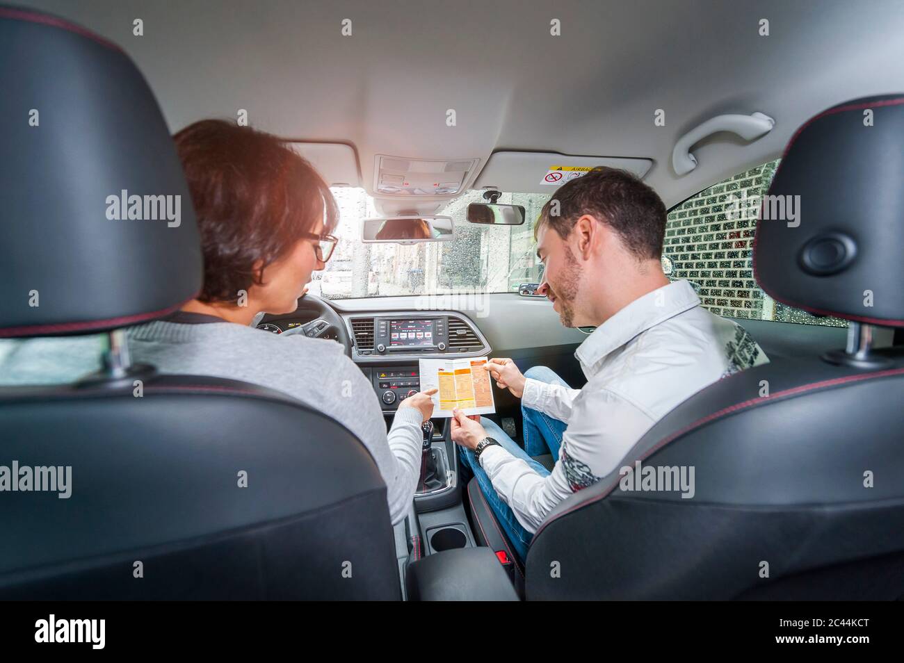 Una conductora aprendiz con una instructora en el coche mirando el guión de la prueba Foto de stock