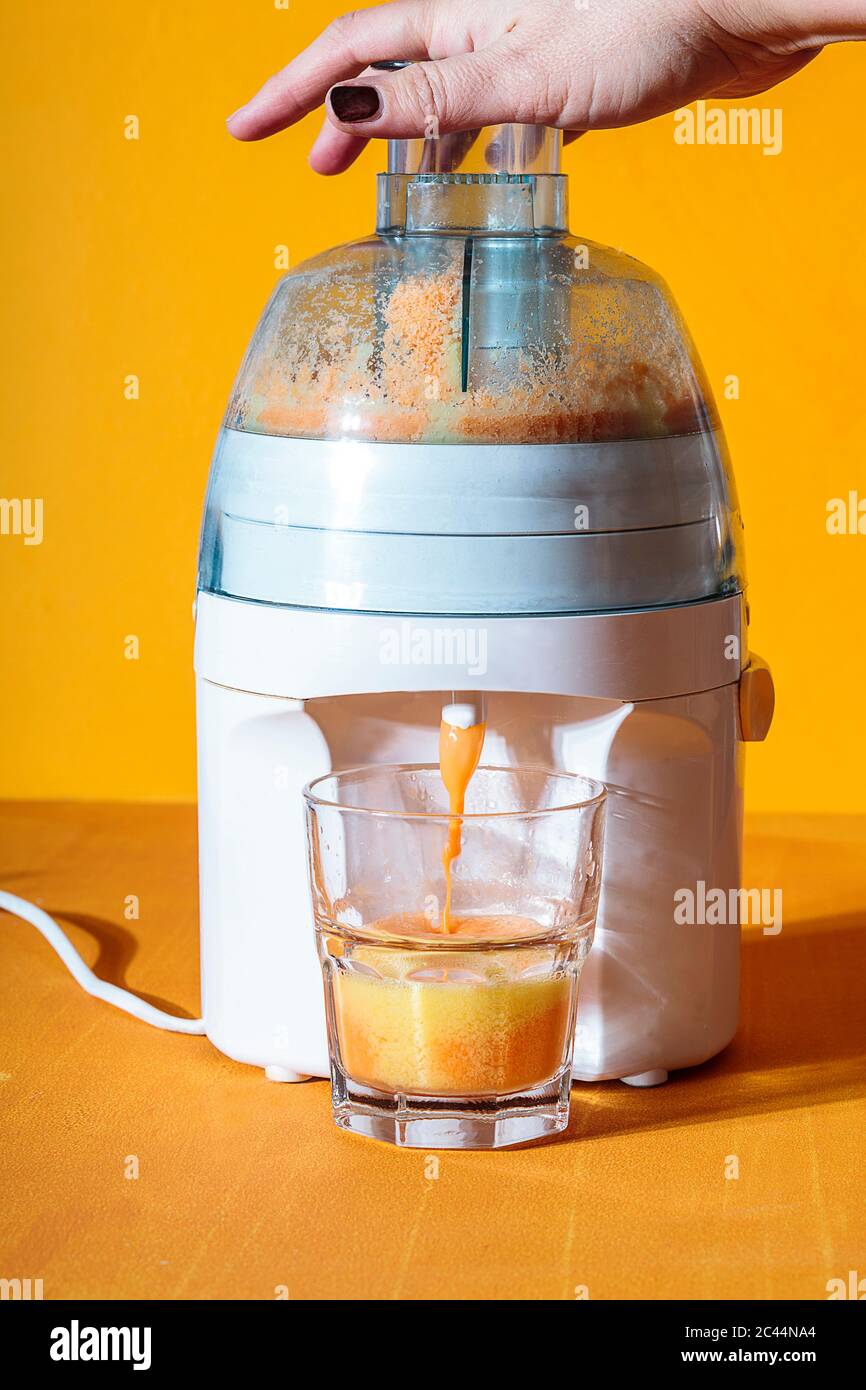 Lado femenino descansa encima de la licuadora verter en el vaso de jugo de zanahoria Foto de stock