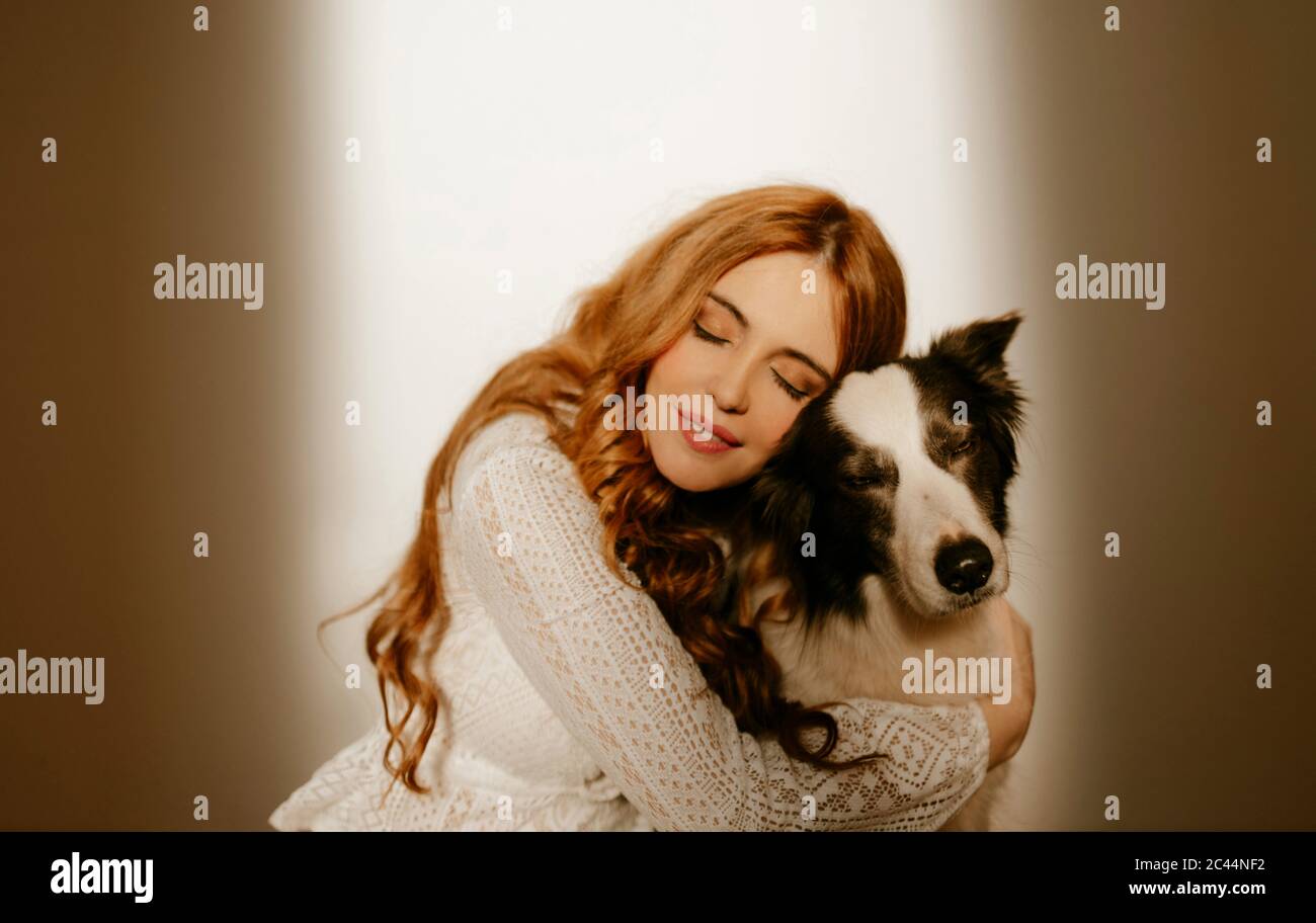 Mujer rubia en casa en pijama abrazando a su perro de collie de la frontera Foto de stock