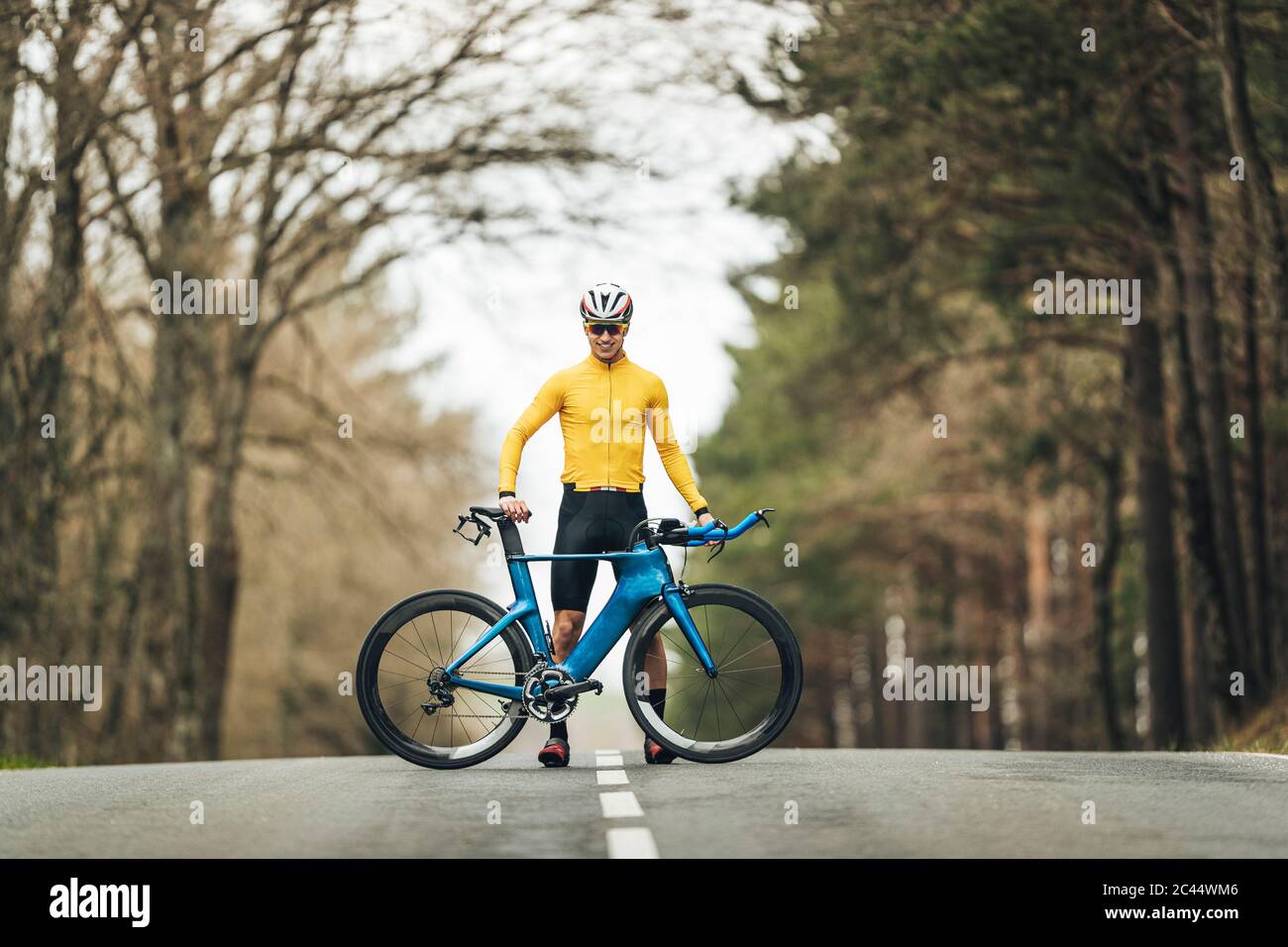 Joven sonriente con ropa deportiva de pie con bicicleta de montaña en carretera Foto de stock