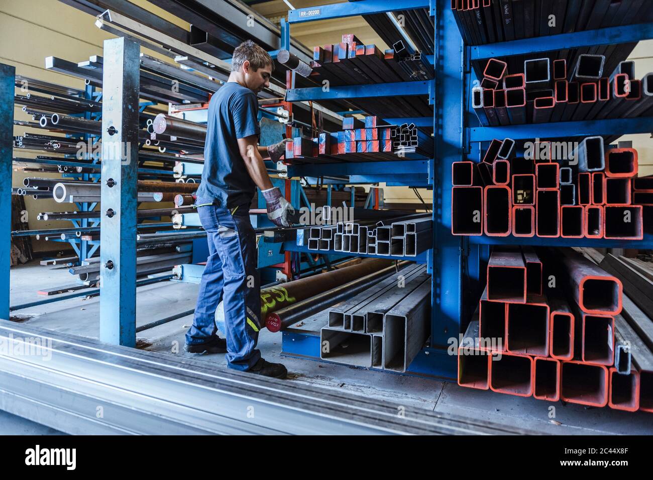 Hombre trabajando con barras de metal en un estante en una fábrica Foto de stock