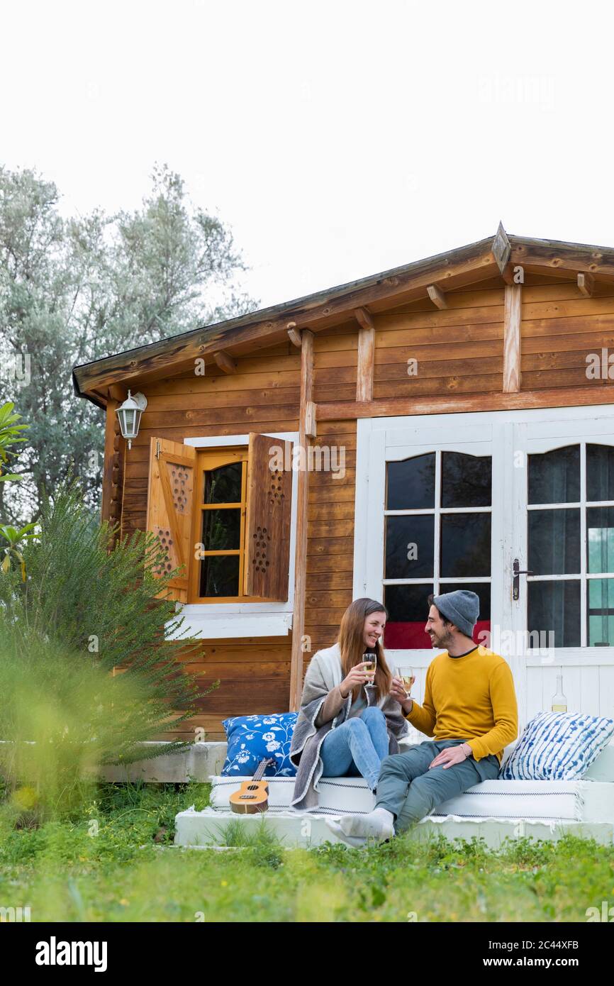 Feliz pareja sosteniendo wineglasses hablando mientras se sienta en los  escalones de la cabaña de madera Fotografía de stock - Alamy