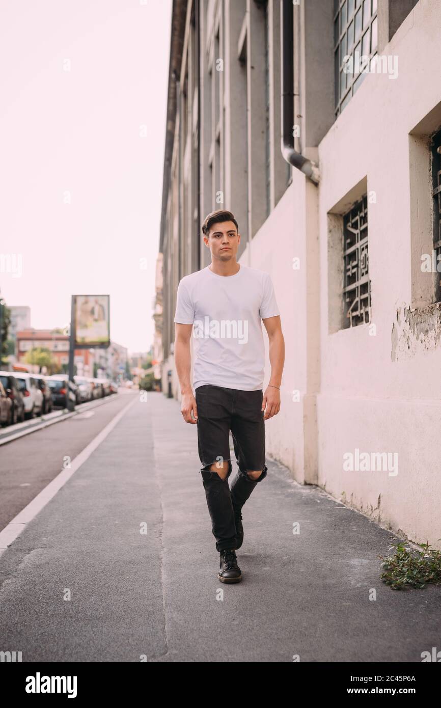 Retrato un joven con pelo marrón oscuro, con camiseta blanca y jeans negros rasgados, caminando por calle Fotografía de stock - Alamy