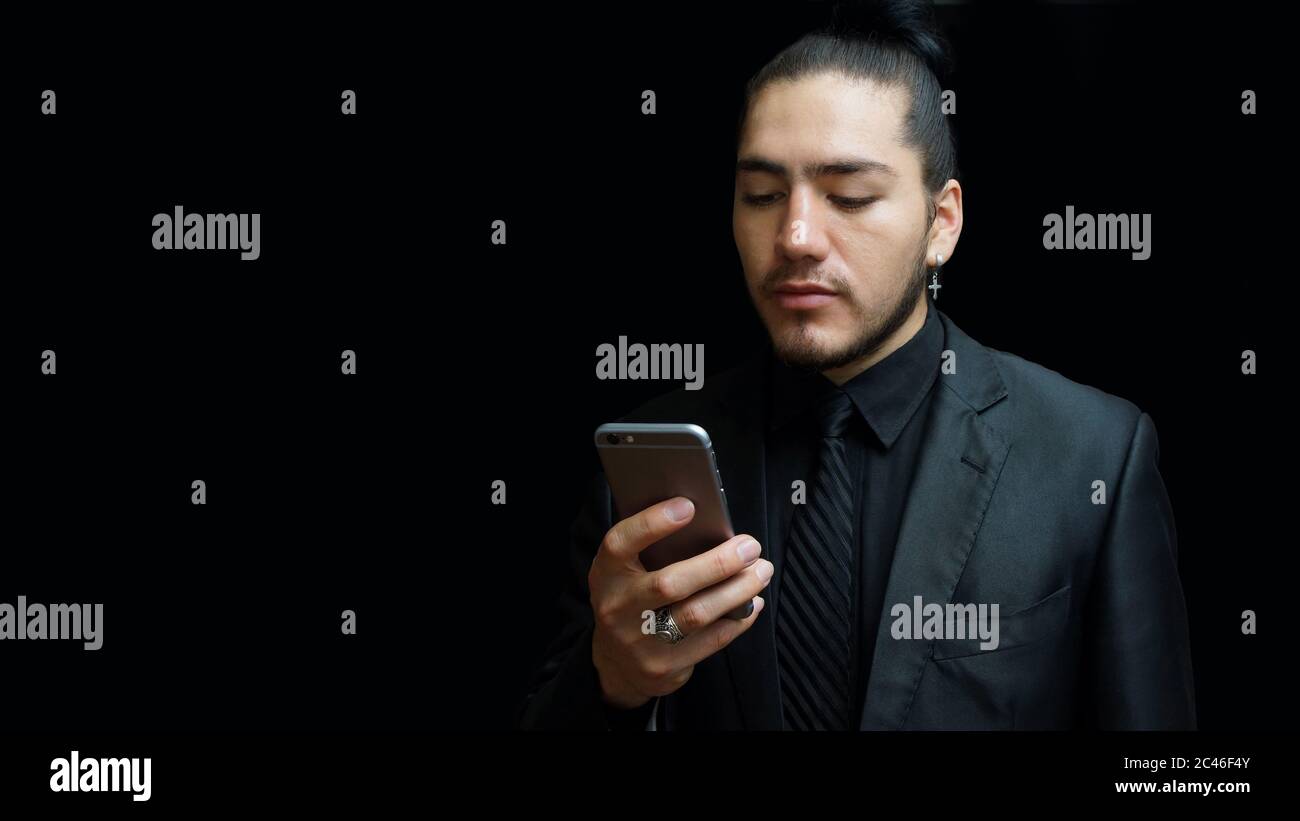 Joven latino en traje negro, camisa negra, corbata negra mirando un