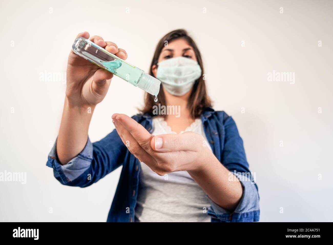 Mujer con máscara de protección médica poniendo antiséptico para desinfectar sus manos Foto de stock