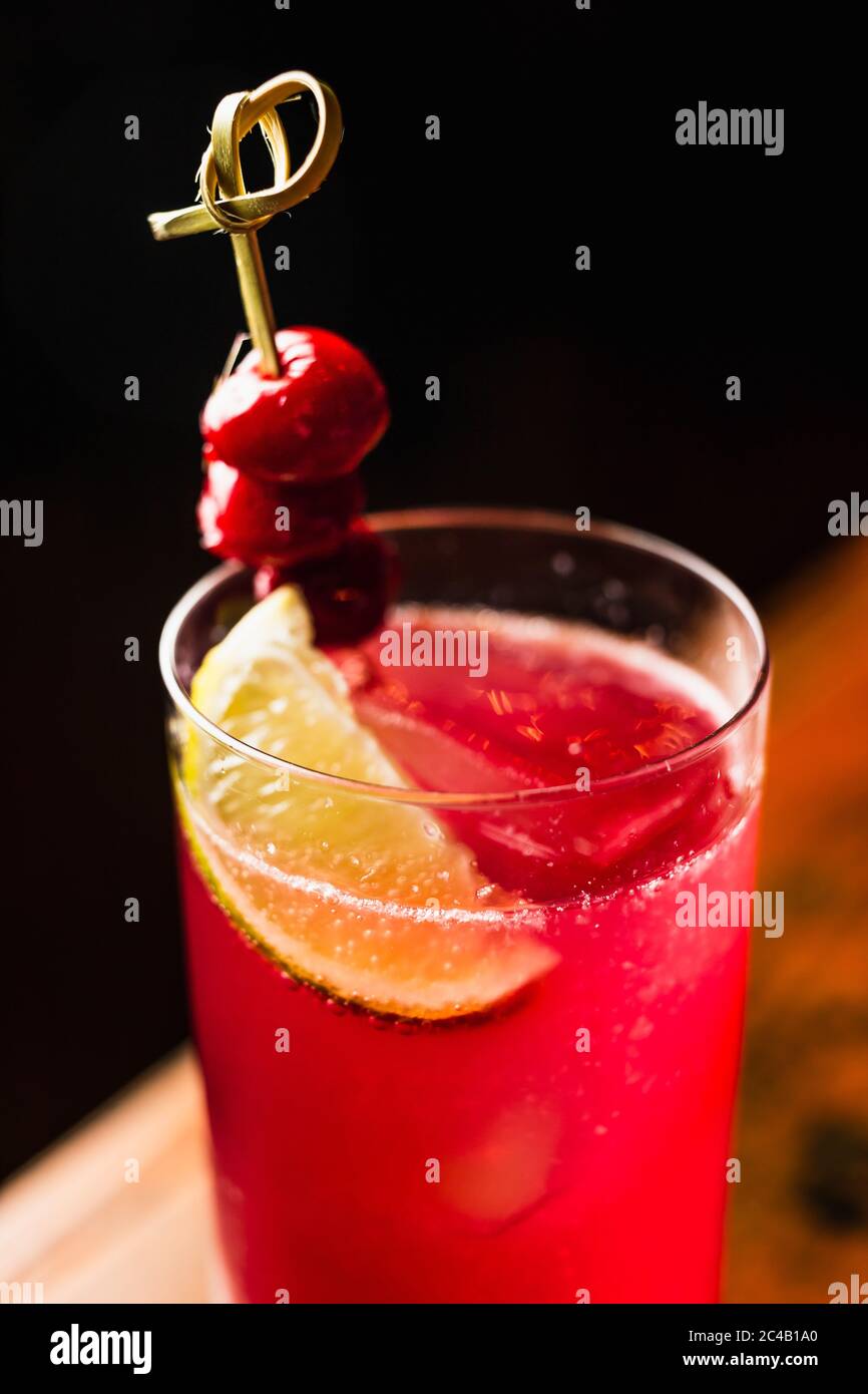 Un cóctel rojo en un vaso de bola alta adornada con limón y cerezas Foto de stock