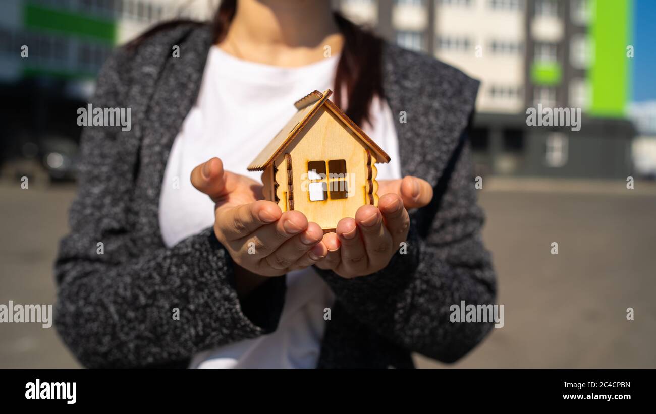Cerca de la mujer sosteniendo una pequeña casa de madera en las manos sobre el fondo de la casa construida. Concepto de compra de nuevo apartamento. Foto de stock