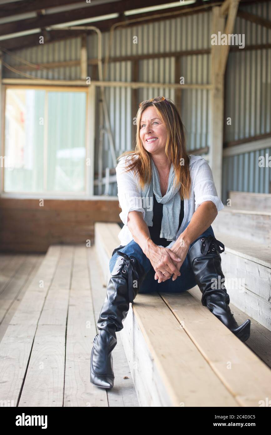 Retrato atractiva mujer madura sentada relajada confiada soñando despierto  en banco, feliz sonriendo, en jeans, blusa y botas de tacón alto de aguja  Fotografía de stock - Alamy