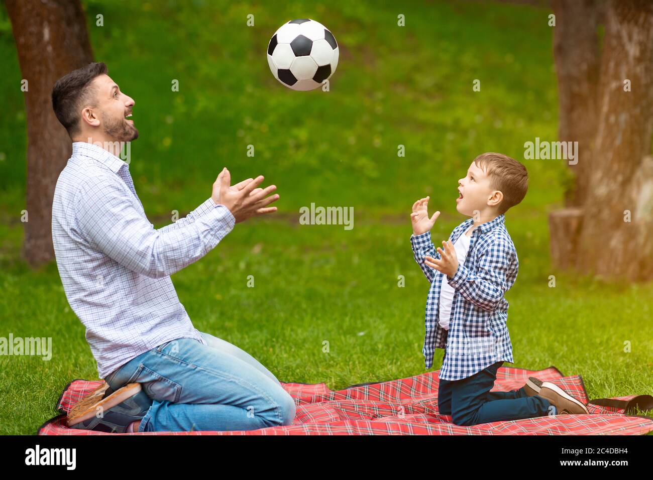 Actividades familiares en verano. Adorable chico con padre jugando al fútbol juntos en un picnic en el bosque Foto de stock