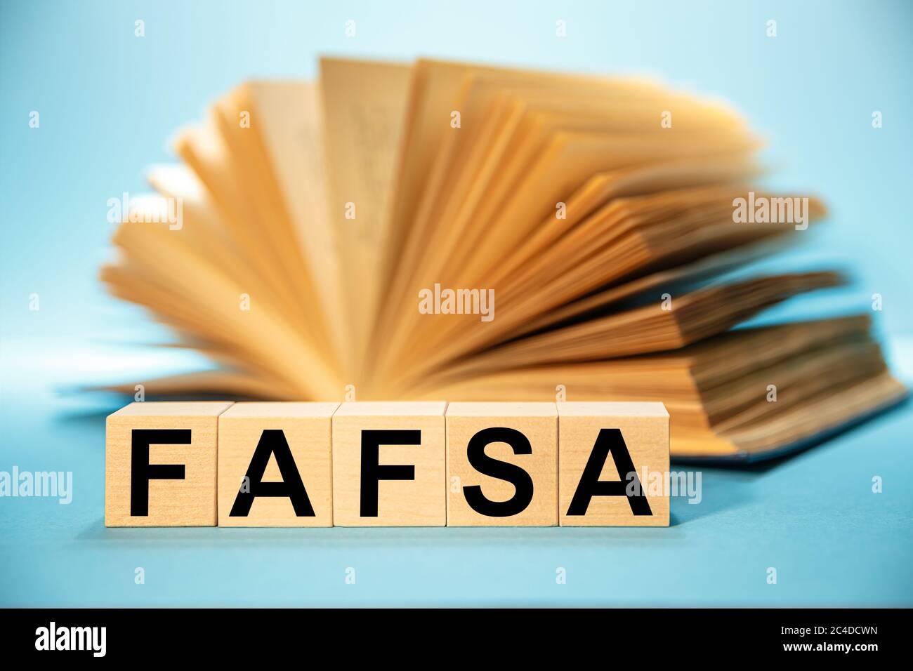 Cubos de madera con la abreviatura solicitud gratuita de ayuda federal para estudiantes FAFSA en el fondo de un libro abierto. Foto de stock
