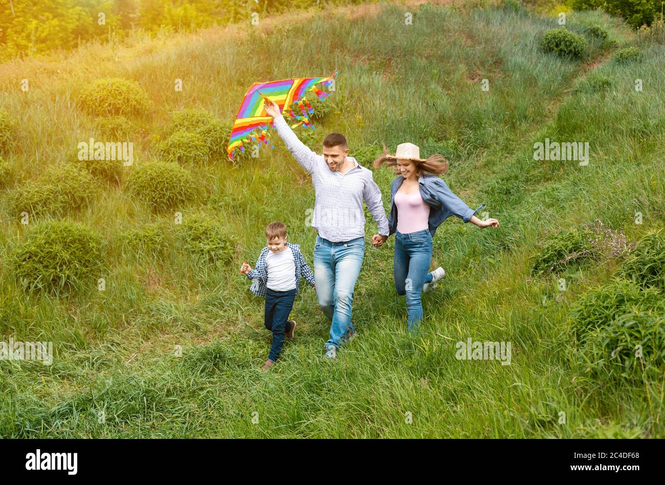 Actividades familiares de verano. Padres jóvenes alegres con su hijo volando cometas juntos en el campo Foto de stock