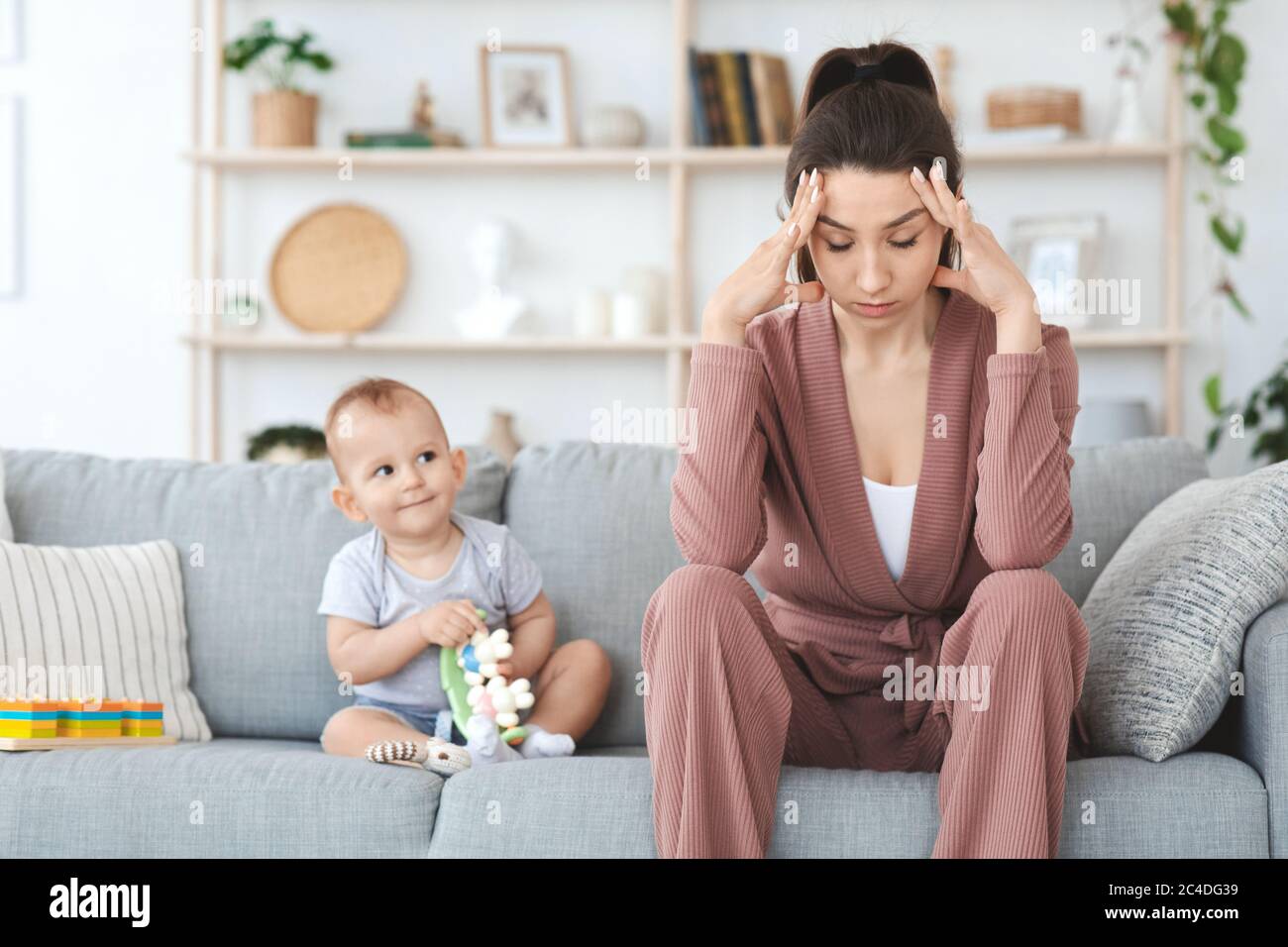 Estrés de la maternidad. Mujer joven deprimida sentada con un bebé en casa Foto de stock