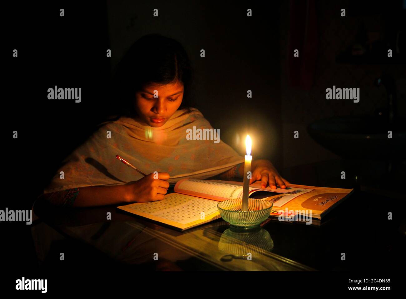 Una niña estudiando en casa con velas después de que la carga de electricidad se derramara en la ciudad de Dhaka, Bnagladesh. Apagón. Problema de electricidad. Foto de stock