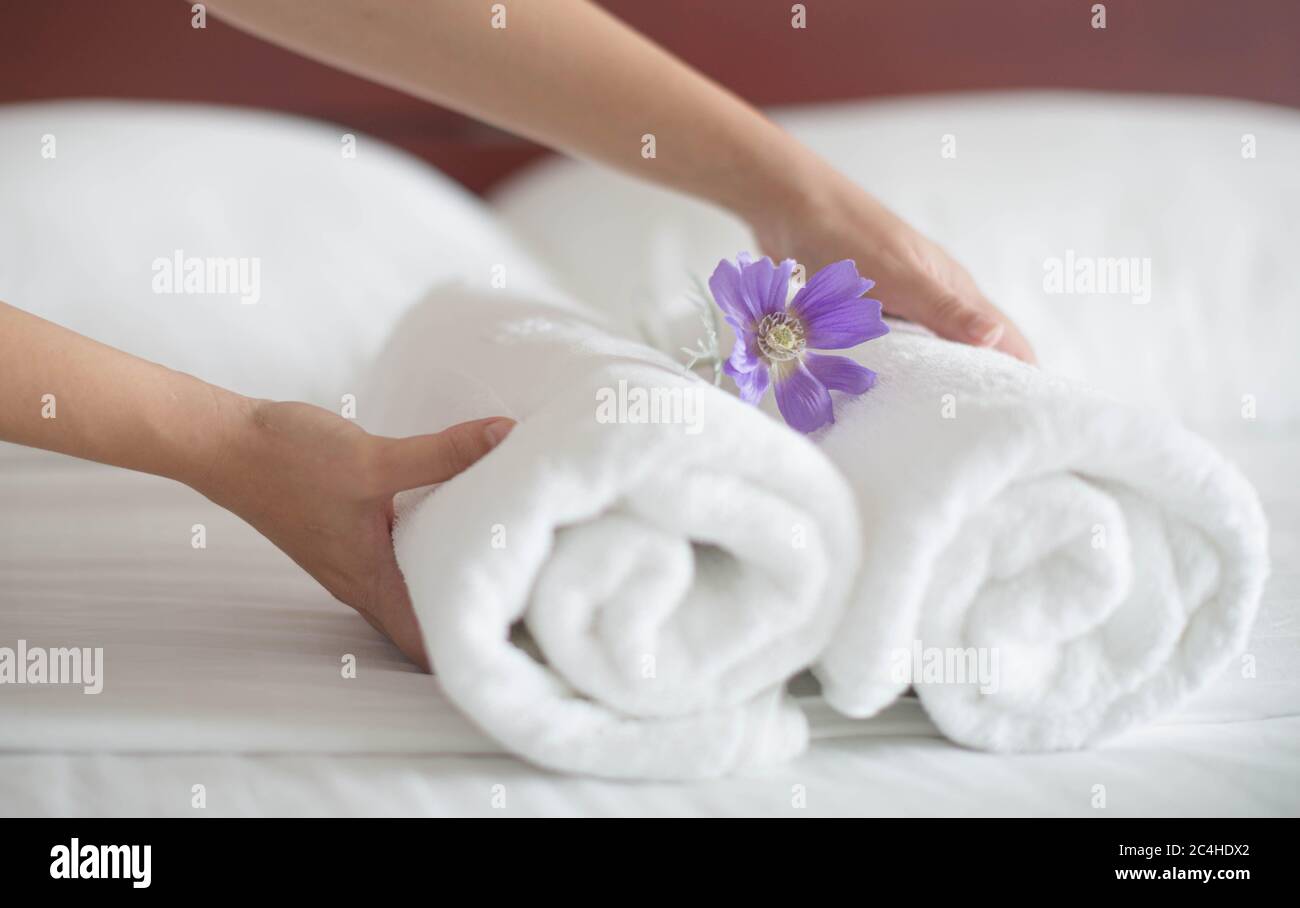 La camarera de piso pone un juego de toallas blancas y una flor en una cama de hotel. Foto de stock