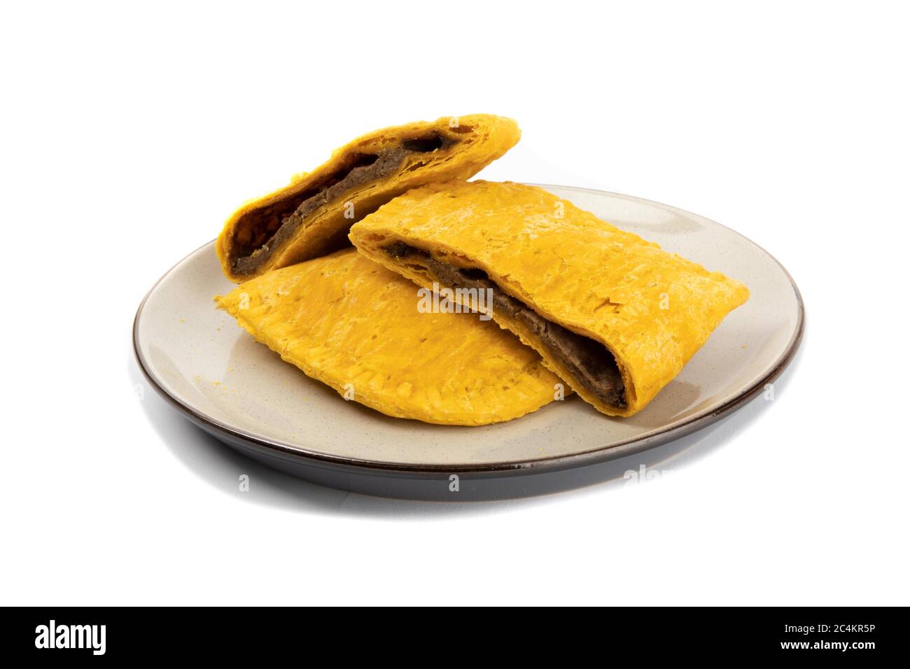 Corte las empanadas picantes de la carne jamaicana o de las Indias Occidentales en un plato aislado en blanco Foto de stock