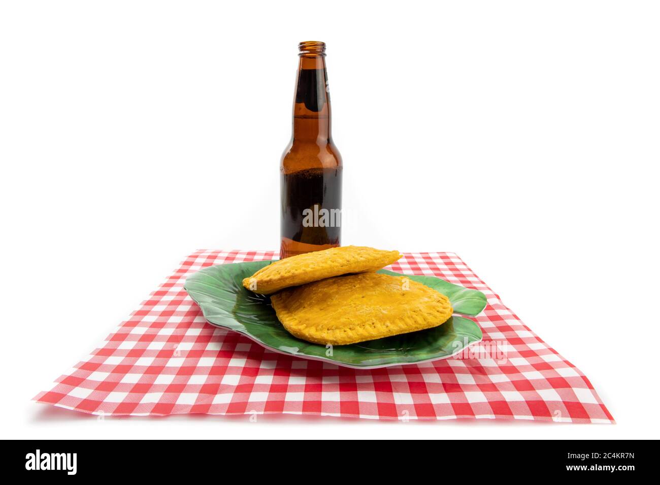 Dos empanadas jamaiquanas en un papel de cuadros rojo y blanco con una botella de cerveza no identificada Foto de stock
