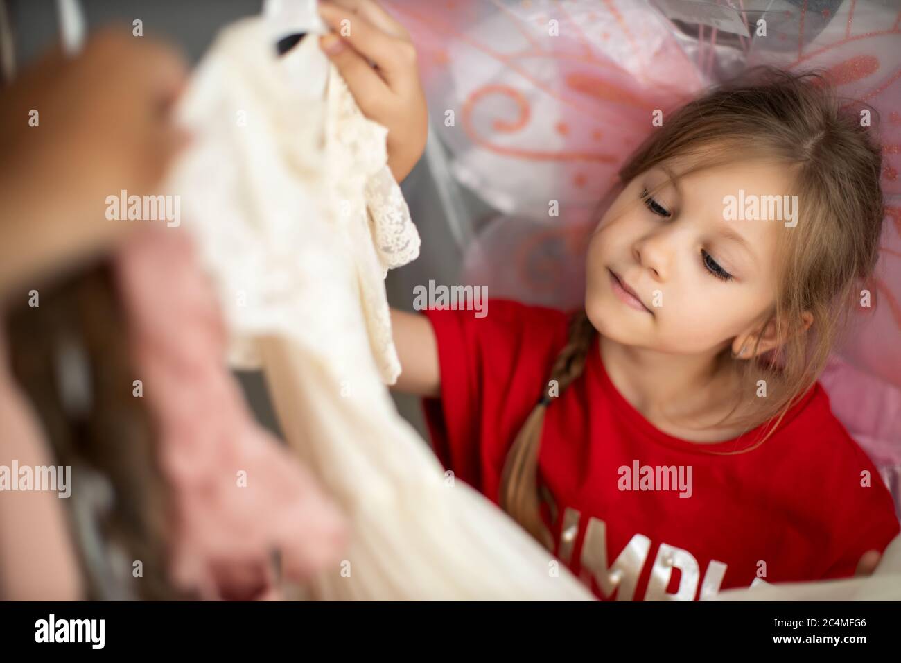 Una chica de preescolar ha elegido un nuevo vestido encantador entre un montón de ropa en la tienda de moda infantil Foto de stock