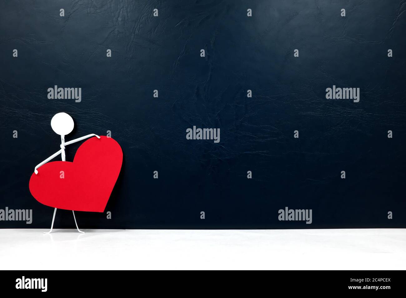Figura de palo humano que sostiene un corazón rojo grande en fondo oscuro. Dar amor y solo valentines día de celebración concepto. Foto de stock