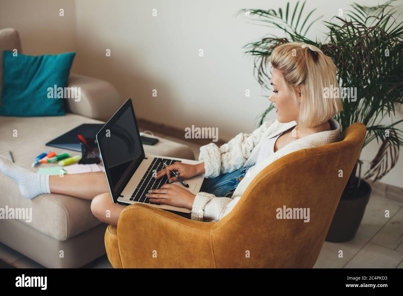 Mujer caucásica ocupada con cabello rubio charlando en el portátil y haciendo tareas en casa en línea Foto de stock