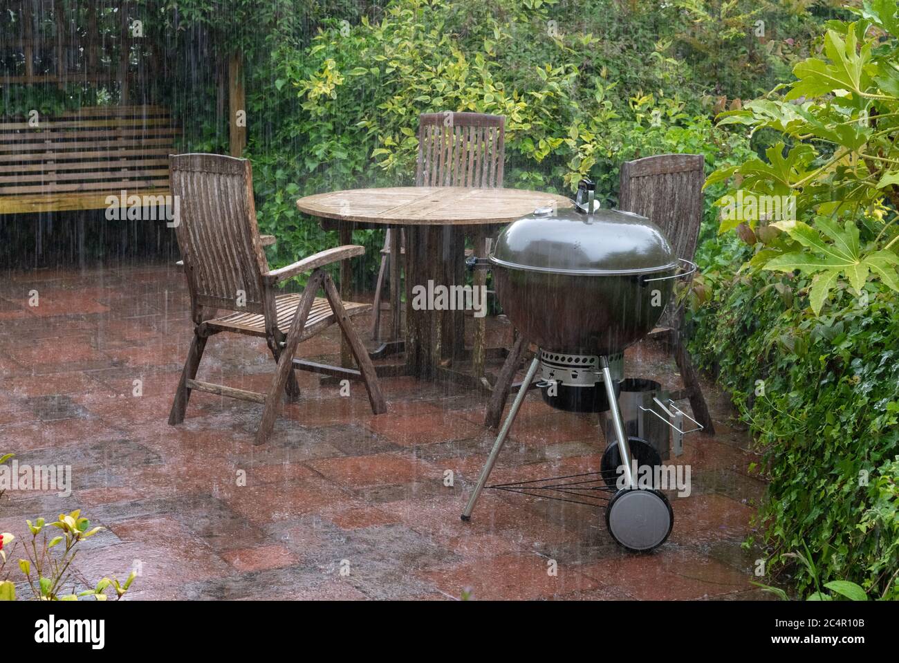 Fuerte lluvia de verano cayendo en el jardín de muebles de patio y barbacoa en junio, Escocia, Reino Unido Foto de stock