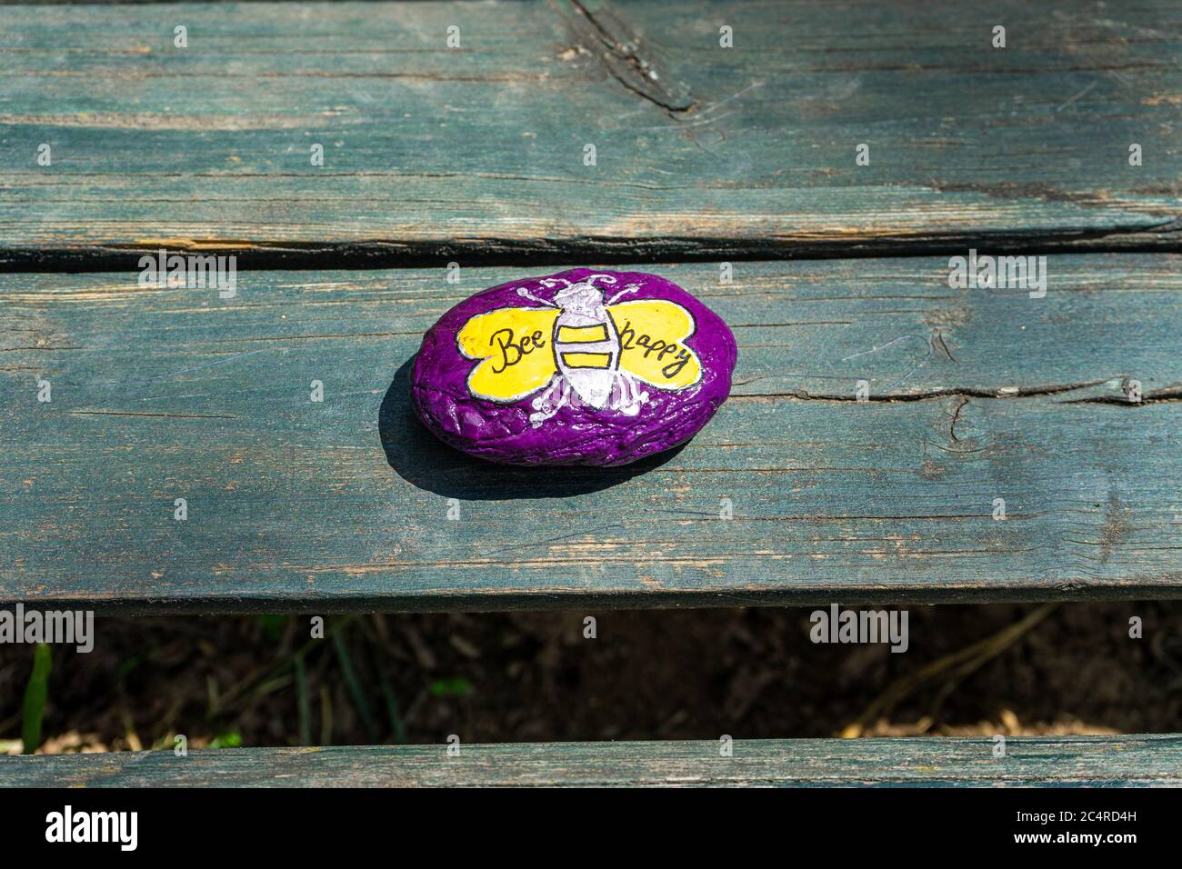 Pebble pintado de color púrpura con UN LOGOTIPO de Bees en un banco en Baja Baviera Alemania Foto de stock