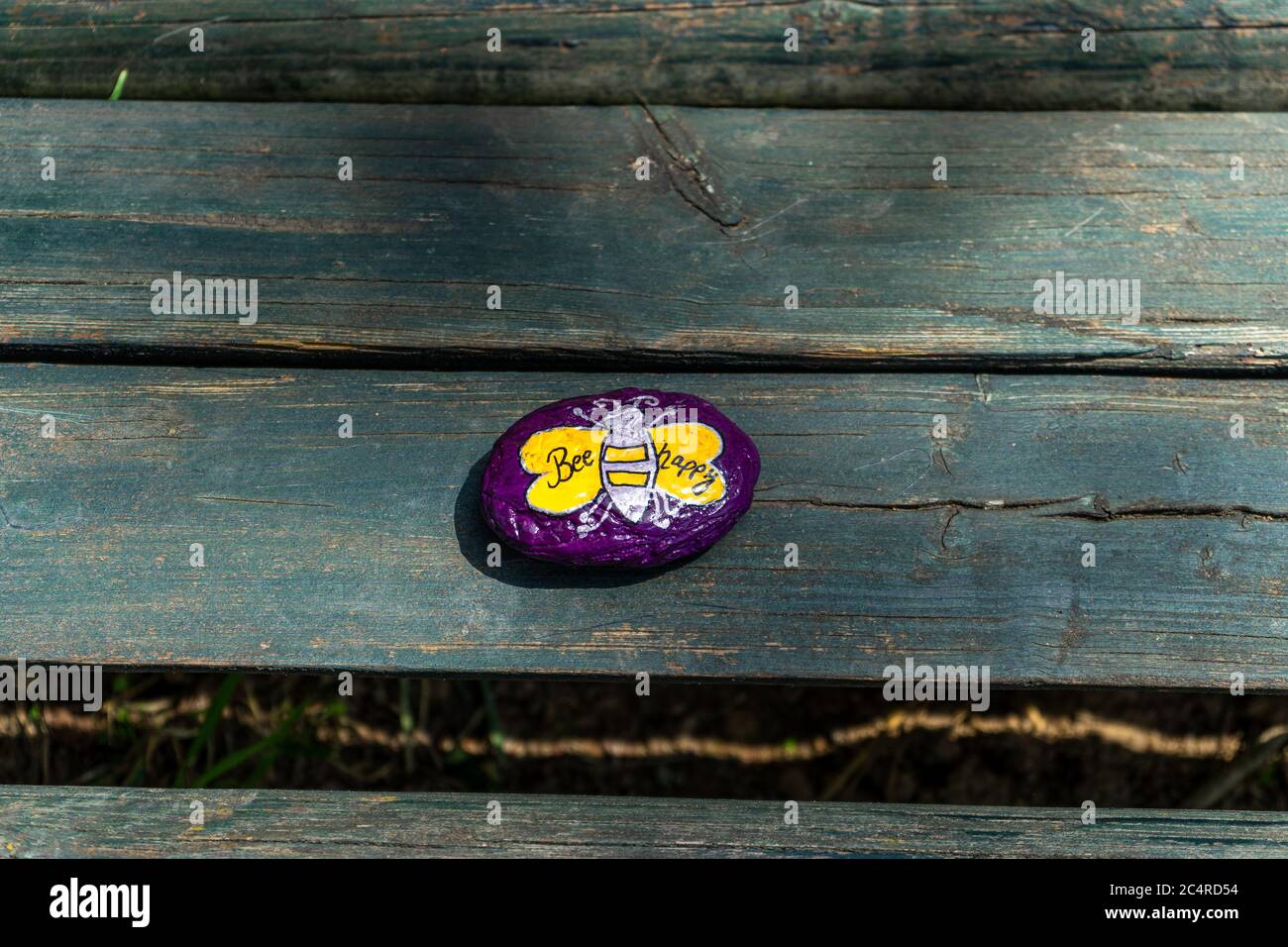 Pebble pintado de color púrpura con UN LOGOTIPO de Bees en un banco en Baja Baviera Alemania Foto de stock