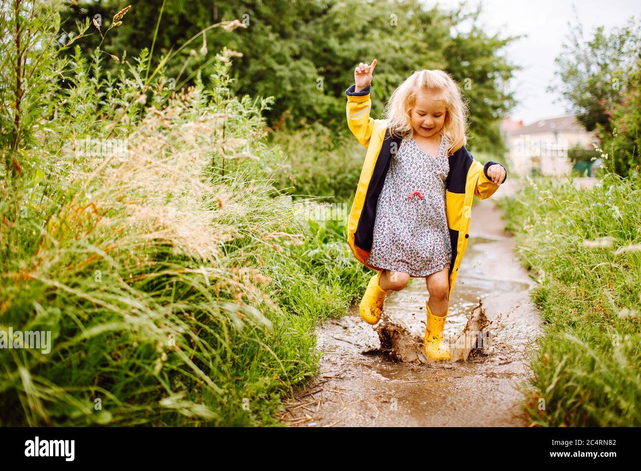 Feliz rubia niña en un amarillo botas de goma y impermeable amarillo  saltando en un charco. Verano, infancia, vacaciones Fotografía de stock -  Alamy