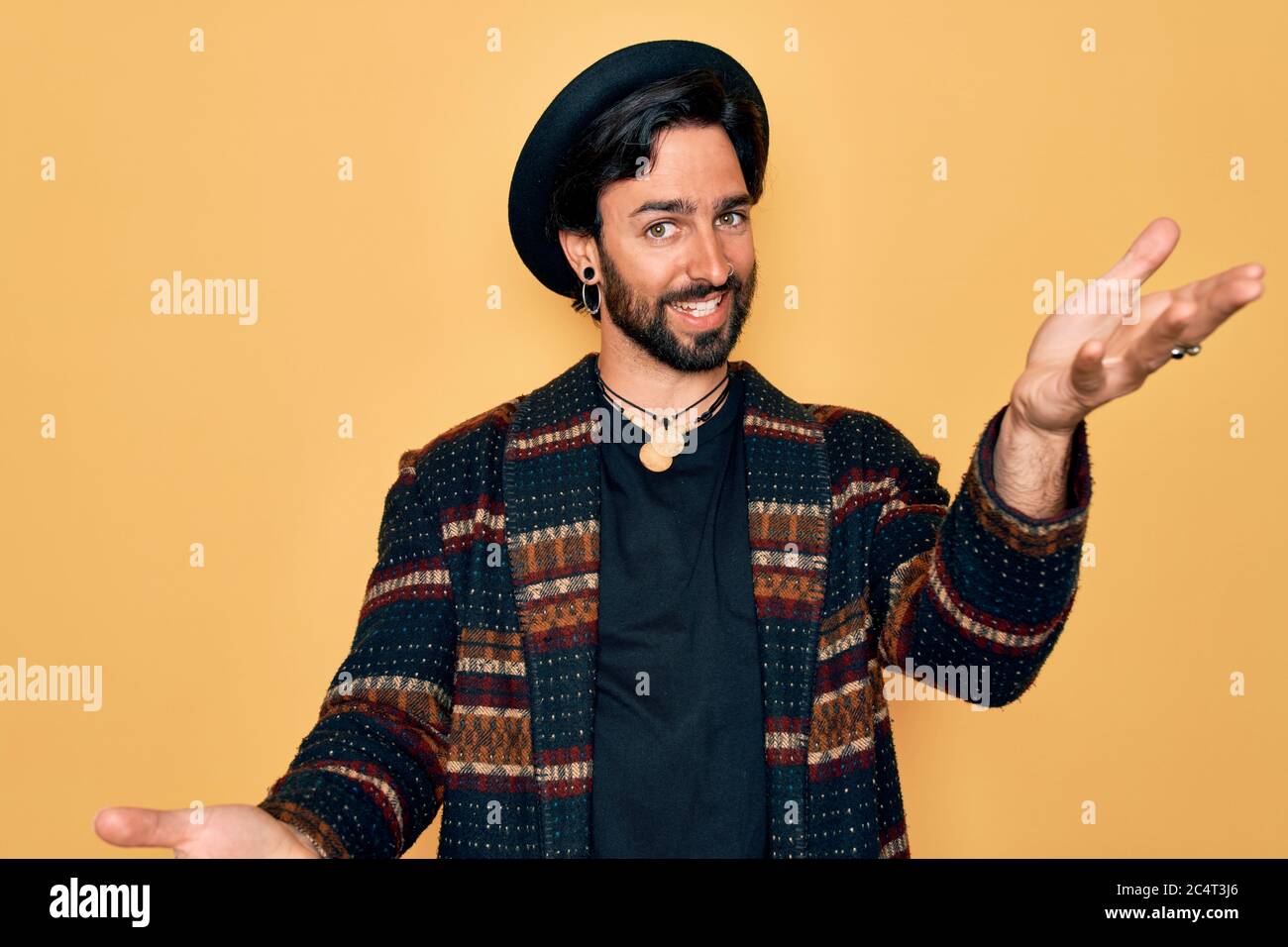 Joven hombre bohemio hispano guapo con estilo hippie y sombrero boho sonriendo ofreciendo manos dando asistencia aceptación Fotografía stock - Alamy