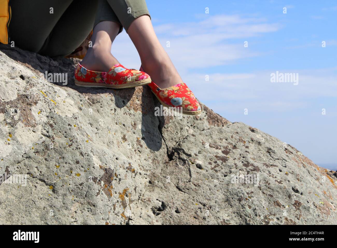 Piernas de una chica que se sienta en una montaña alta contra un cielo azul Foto de stock