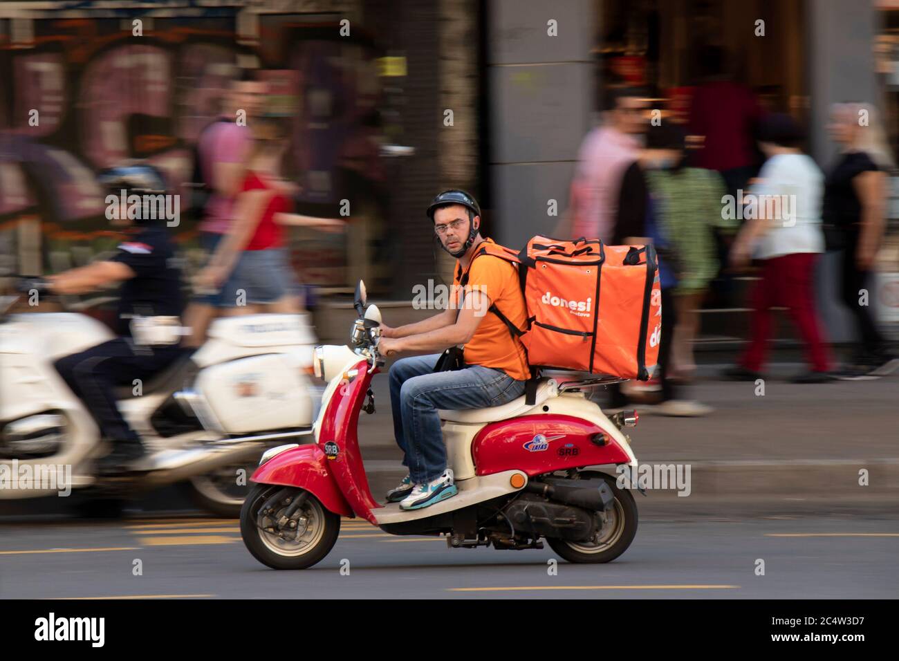 Belgrado, Serbia - 25 de junio de 2020 : Servicio de entrega mensajero montando un dos tonos rojo beige vespa scooter vintage en el tráfico urbano, barrido Foto de stock
